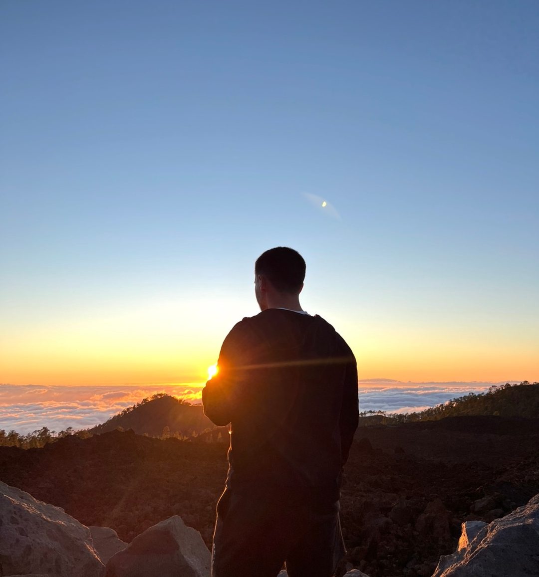 Daniel, seen from behind, on a ridge above cloud at sunrise.